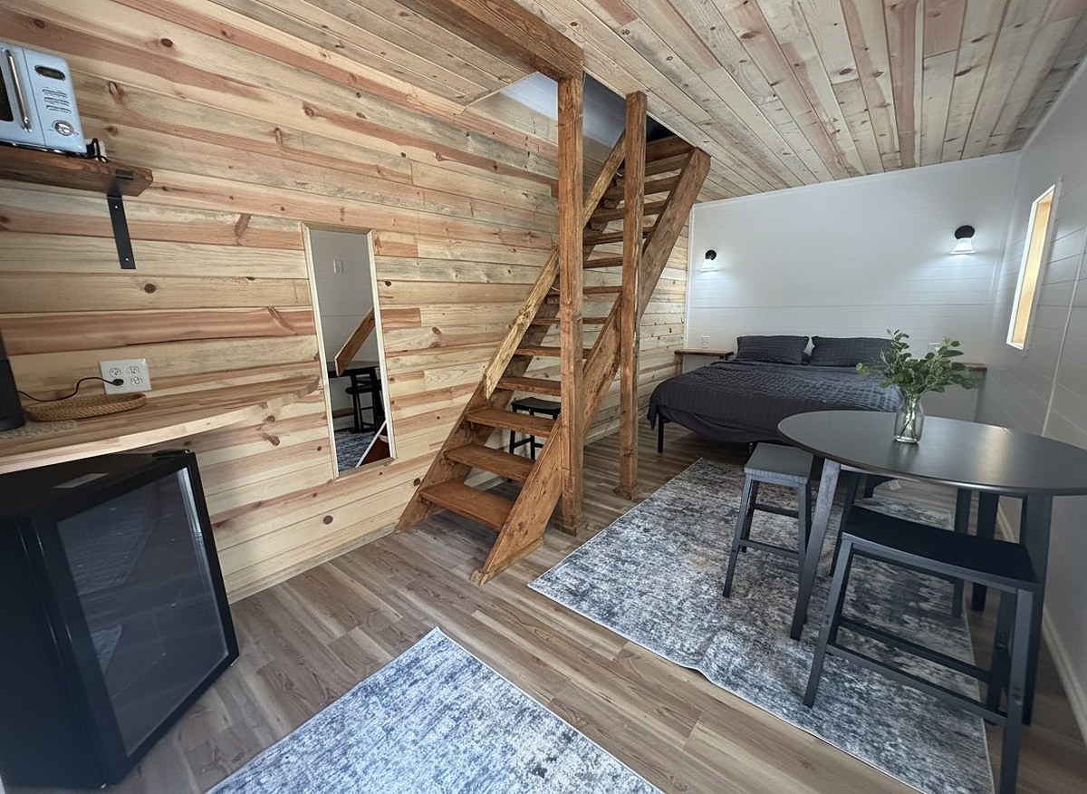 Inside The Caribou — cedar plank walls, a timber loft staircase, queen bed and round dining table