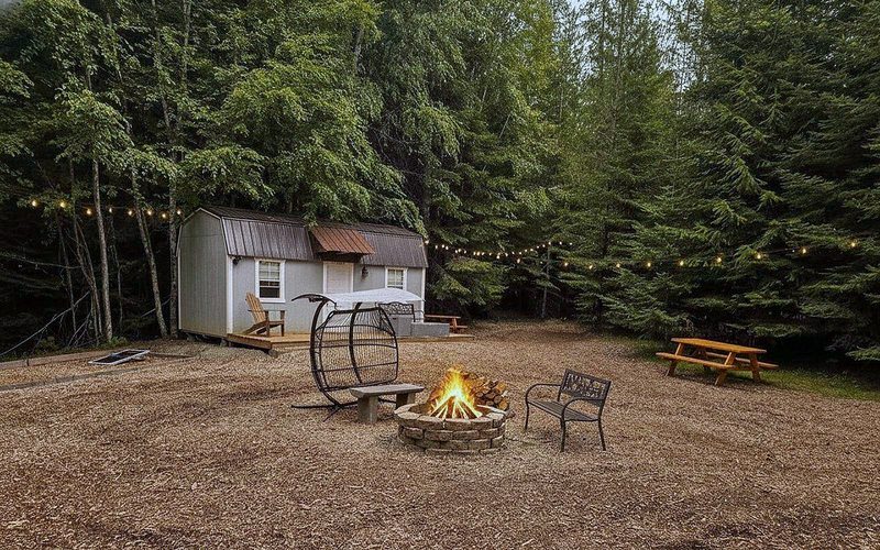 A fire burning in the stone fire ring at the heart of the cabin village at Round Mountain Retreat, string lights glowing in the pines at dusk.